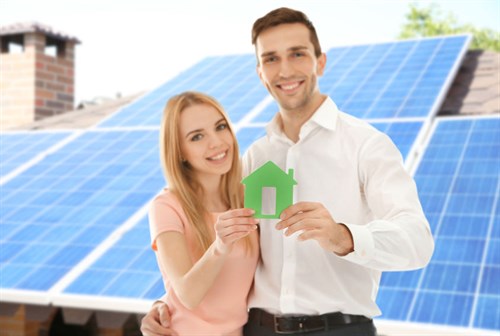 Happy couple holding figure of house and solar panels on background