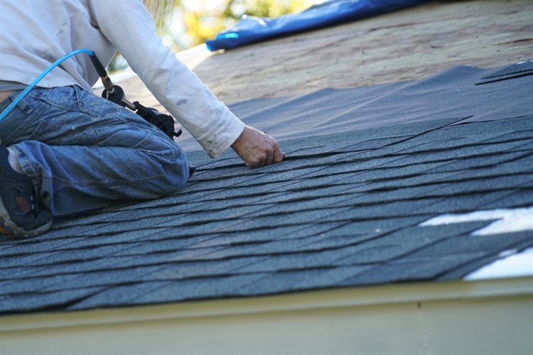 Image of a man replacing shingles on a roof.